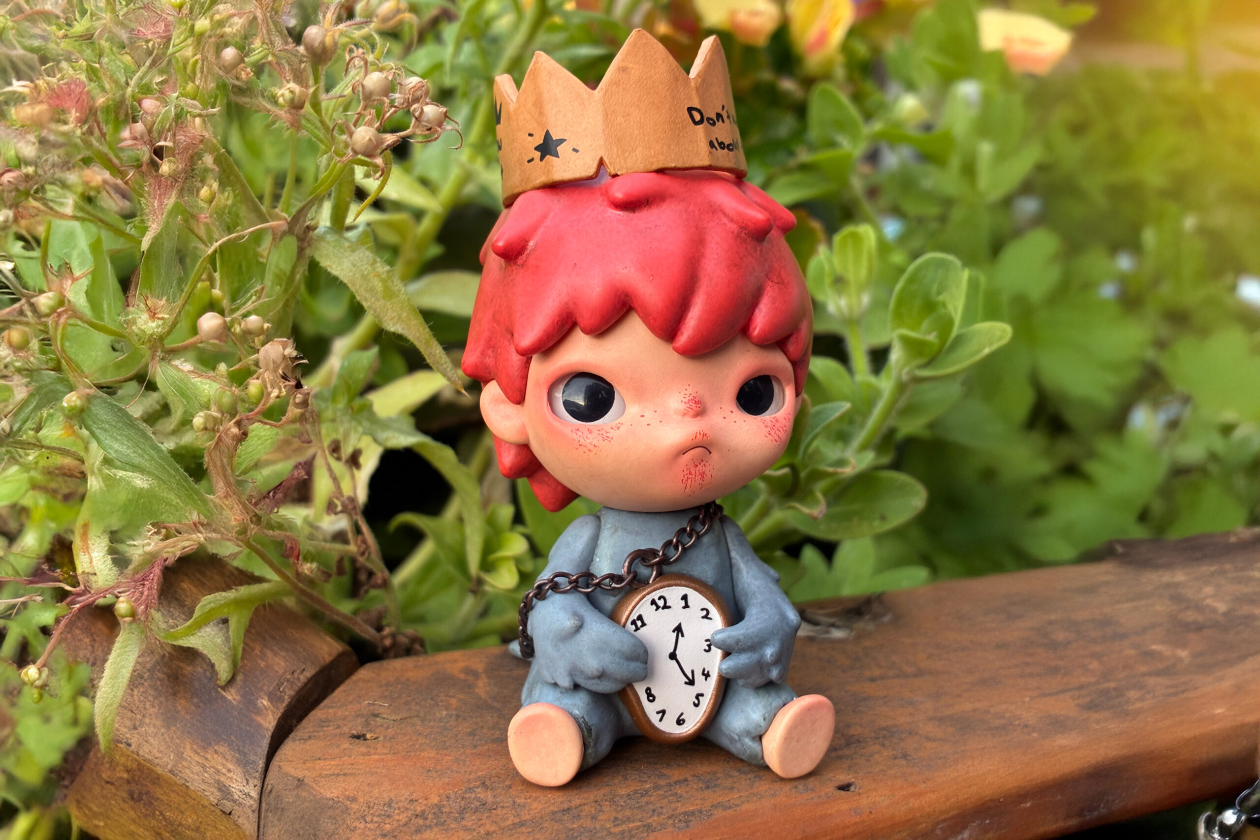 hirono pop mart figurine, super cute and small, siting down outside behind leaves.